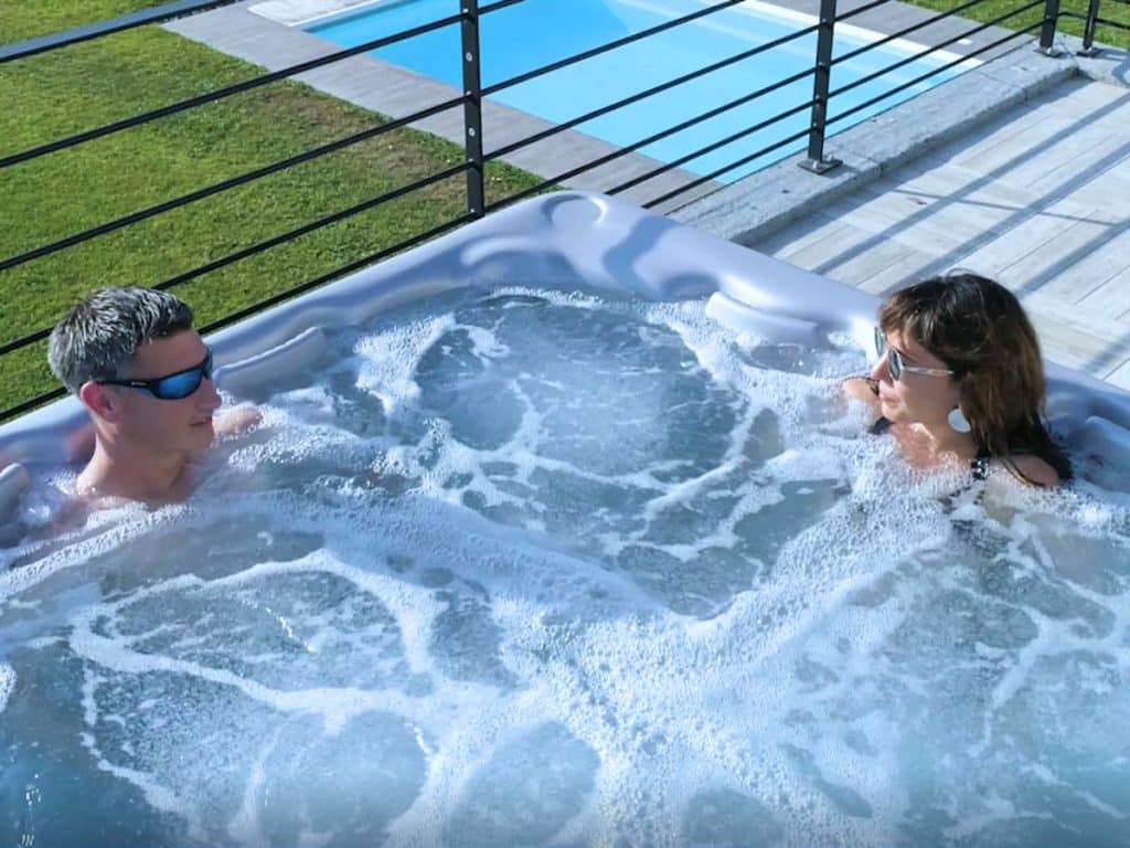 Homme et femme qui se détendent dans un spa à domicile avec piscine en arrière plan